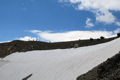 hikers crossing the ridge above a snow bank