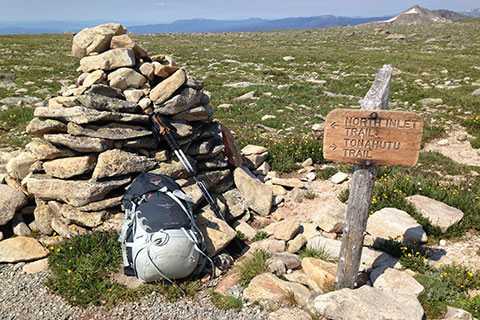 Junction trail sign near large cairn on Flattop Mountain. A pack and poles lay against the cairn.