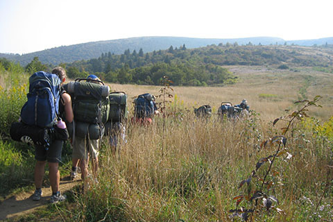 students backpacking through tall grass