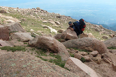 Hiker carrying two packs struggling on the upper slopes of Pikes Peak